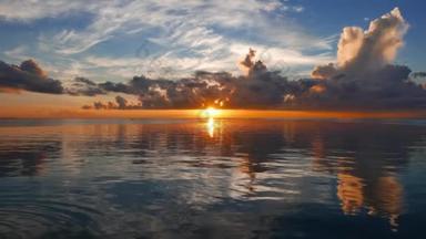 一个非常丰富多彩的日出视频从杜马格特城市海岸与镜子一样的海洋。太阳可以在地平线上看到。用缓慢的平移相机拍摄.